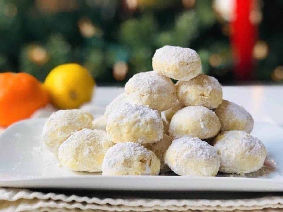 Snowball cookies piled up into a pyramid shape on a white plate with an orange and lemon in the background.