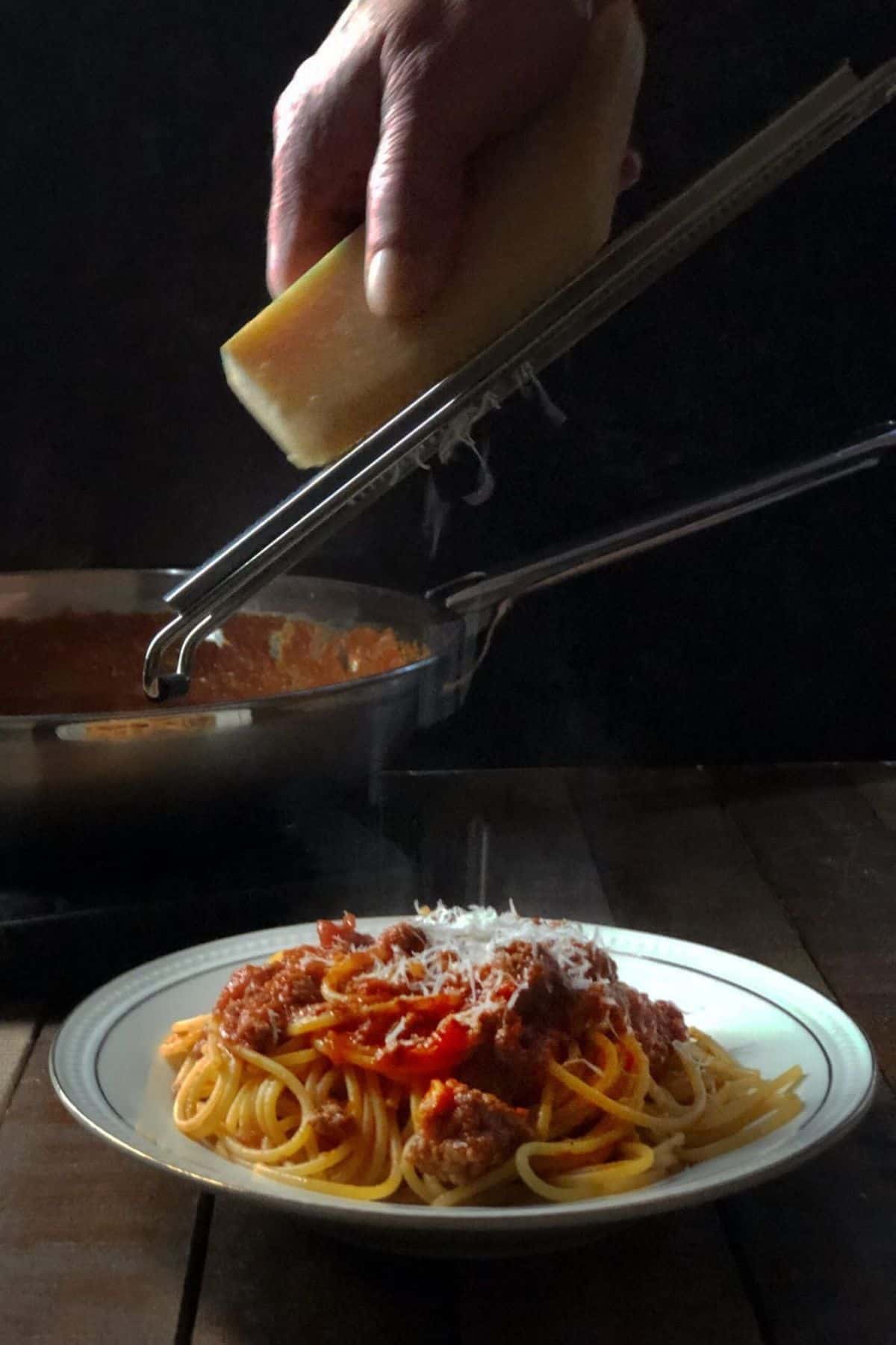 Pork Bolognese in a bowl with Parmesan cheese shredded on top.