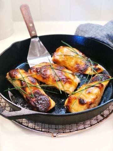 A zoomed in view of four baked miso salmon filets in a cast iron pan with a spatula in the pan and chives on top sitting on the counter.