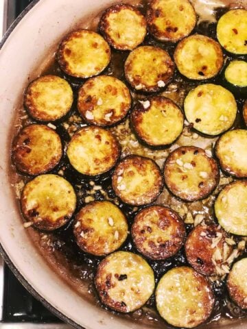 Zucchini slices in a pan with brown butter and minced garlic on top.