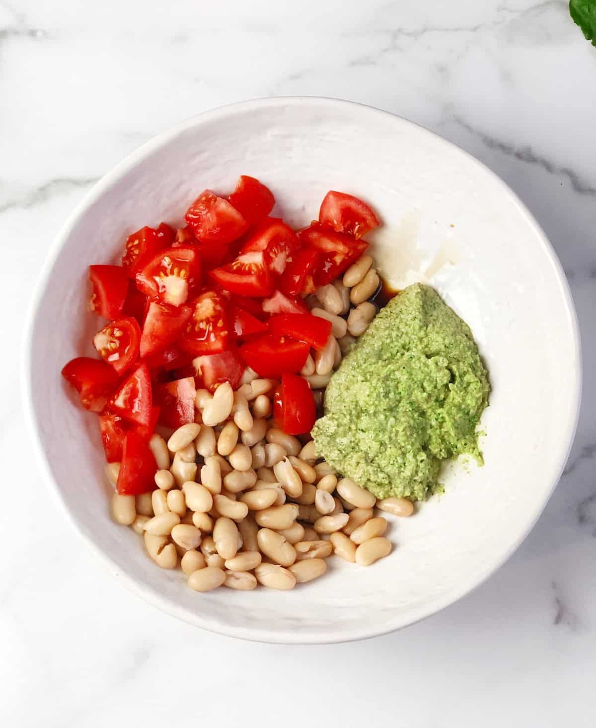 Pesto pasta ingredients in a large bowl to be tossed together.