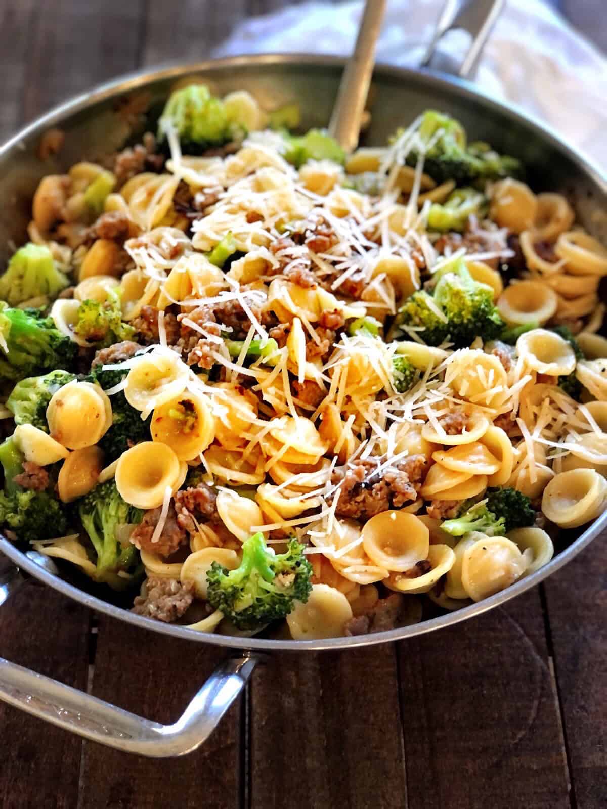 Orecchiette with sausage and broccoli in a large saute pan on a wood table.