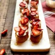 Crostini with goat cheese and balsamic strawberries on top on a long plate.