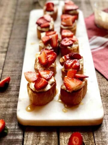 Crostini with goat cheese and balsamic strawberries on top on a long plate.