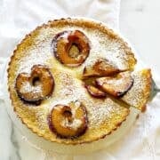 Italian plum and custard tart in a round tart pan on a white counter.
