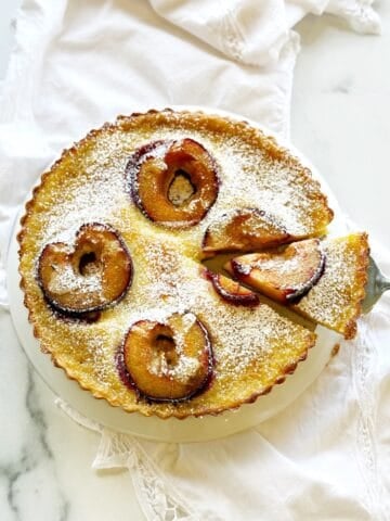 Italian plum and custard tart in a round tart pan on a white counter.