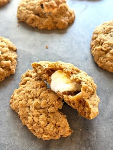 Oatmeal cookies stuffed with marshmallows on the counter with the cookie cut in half to show the marshmallow inside.