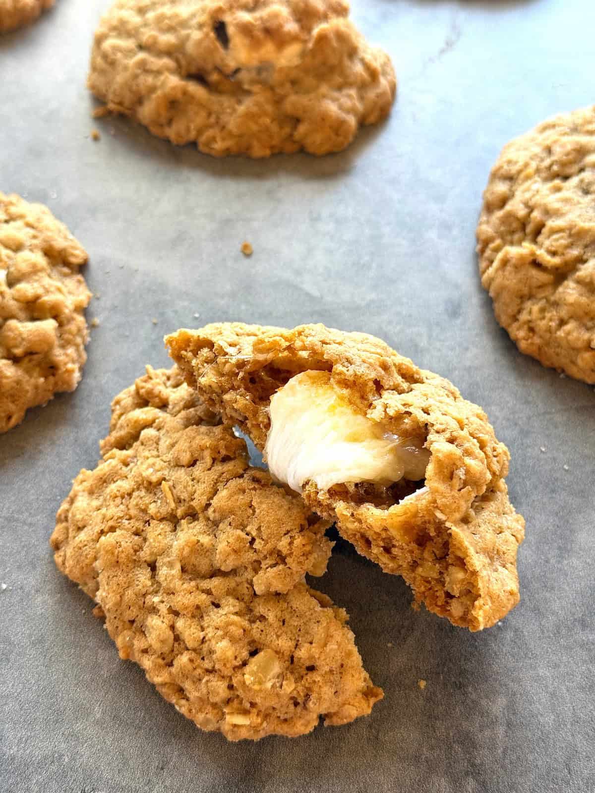 Oatmeal cookies stuffed with marshmallows on the counter with the cookie cut in half to show the marshmallow inside.