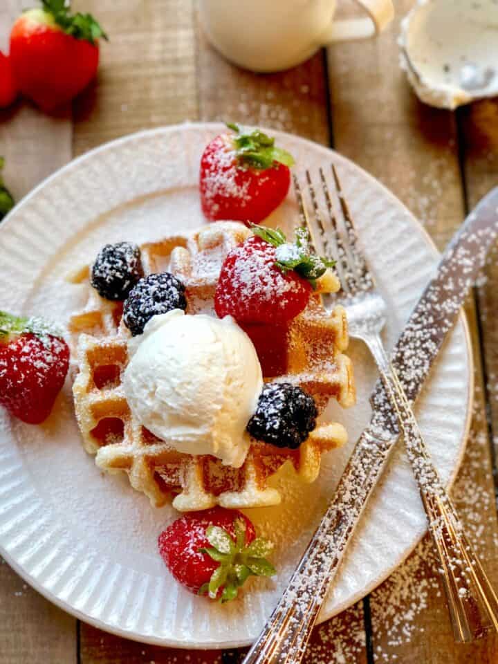Yeasted waffles on a plate with berries and whipped cream.